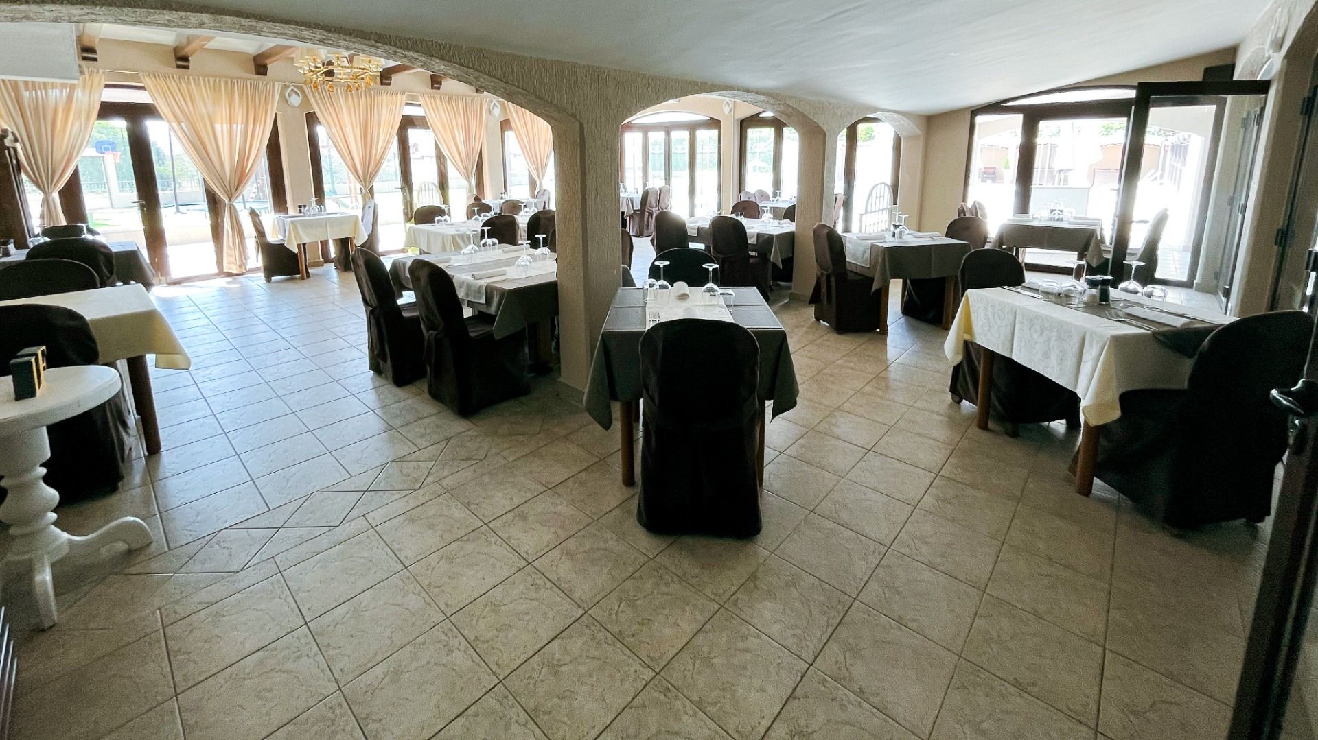 Genießen Sie den geräumigen, sonnendurchfluteten Speisesaal des Hotels Villa Letan mit stilvollen schwarz-weißen Tischdecken, schicken dunklen Stühlen, großen Fenstern und Fliesenböden - ein einladendes Ambiente, das das ausgezeichnete Preis-Leistungs-Ver