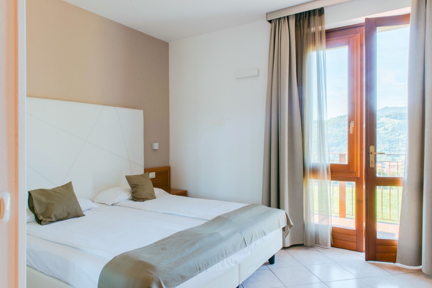 Doppelzimmer mit einem Doppelbett, hellem Interieur, Balkon und Bergblick.