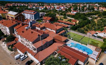 Luftaufnahme der mediterranen Stadt mit dem Hotel Villa Letan, das für seinen Wert bekannt ist und rote Ziegeldächer, einen Pool, einen Sportplatz und üppiges Grün unter einem klaren blauen Himmel aufweist.