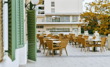 Luftaufnahme des Hotels Lovran mit roten Ziegeldächern, geparkten Autos davor, Bäumen und einem See im Hintergrund an einem sonnigen Tag.