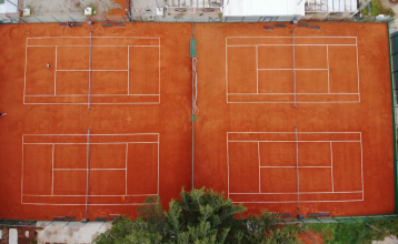 Luftaufnahme der mediterranen Stadt mit dem Hotel Villa Letan, das für seinen Wert bekannt ist und rote Ziegeldächer, einen Pool, einen Sportplatz und üppiges Grün unter einem klaren blauen Himmel aufweist.