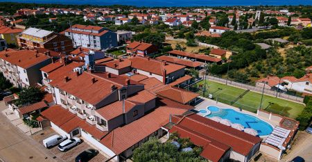 Luftaufnahme der mediterranen Stadt mit dem Hotel Villa Letan, das f&uuml;r seinen Wert bekannt ist und rote Ziegeld&auml;cher, einen Pool, einen Sportplatz und &uuml;ppiges Gr&uuml;n unter einem klaren blauen Himmel aufweist.