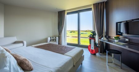 Luftaufnahme der &uuml;ppigen Fairways, Sandbunker, Wasserhindernisse und des markanten Clubhauses mit sechseckigem Dach des Albarella Golf Hotels &ndash; ideal zur Erholung und f&uuml;r eine ruhige Atmosph&auml;re nach dem Sport.