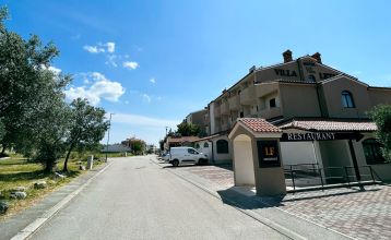 Luftaufnahme der mediterranen Stadt mit dem Hotel Villa Letan, das für seinen Wert bekannt ist und rote Ziegeldächer, einen Pool, einen Sportplatz und üppiges Grün unter einem klaren blauen Himmel aufweist.