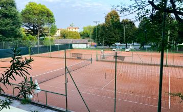 Ein kristallklarer blauer Pool mit Liegestühlen und Sonnenschirmen, umgeben von einer Hecke, mit gelben und roten Häusern und blauem Himmel im Hintergrund – nur eine der entspannenden Kulissen, die Sie im Hotel Donna Silvia genießen können, einem 4-Sterne