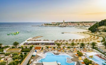 Luftaufnahme des Valamar Padova Hotels 4* – eines Resorts an der Küste mit Pool, Sonnenliegen, Strohsonnenschirmen, Palmen und direktem Zugang zu einem Sandstrand in der Nähe einer historischen Küstenstadt bei Sonnenuntergang. Die Gäste können vielfältige