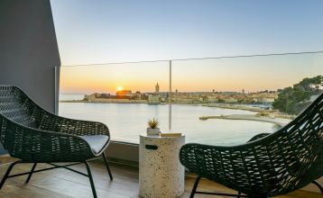 Luftaufnahme des Valamar Padova Hotels 4* – eines Resorts an der Küste mit Pool, Sonnenliegen, Strohsonnenschirmen, Palmen und direktem Zugang zu einem Sandstrand in der Nähe einer historischen Küstenstadt bei Sonnenuntergang. Die Gäste können vielfältige