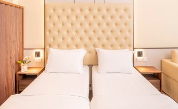 Eingang des Sporthotels Olimpo mit Steinfassade, Hotelname und Sternenmarkierung, umgeben von Pflanzen und Bäumen.