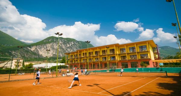 Sand-Tennisplatz mit Spielern, Hotel im Hintergrund und Bergkulisse.