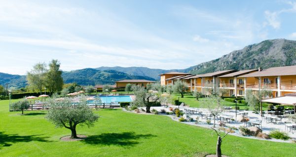 Außenansicht der Hotelanlage La Pertica mit Pool, Sonnenschirmen und Garten, eingebettet in eine Berglandschaft.