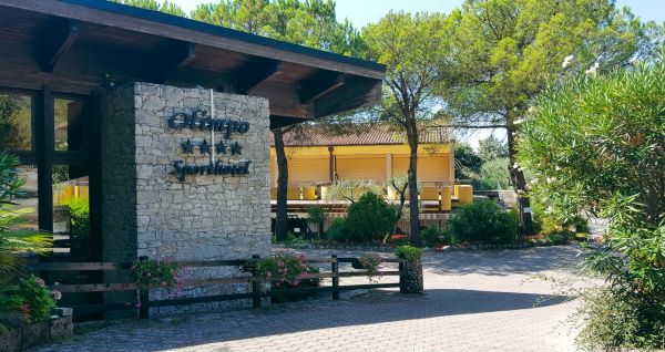 Eingang des Sporthotels Olimpo mit Steinfassade, Hotelname und Sternenmarkierung, umgeben von Pflanzen und Bäumen.
