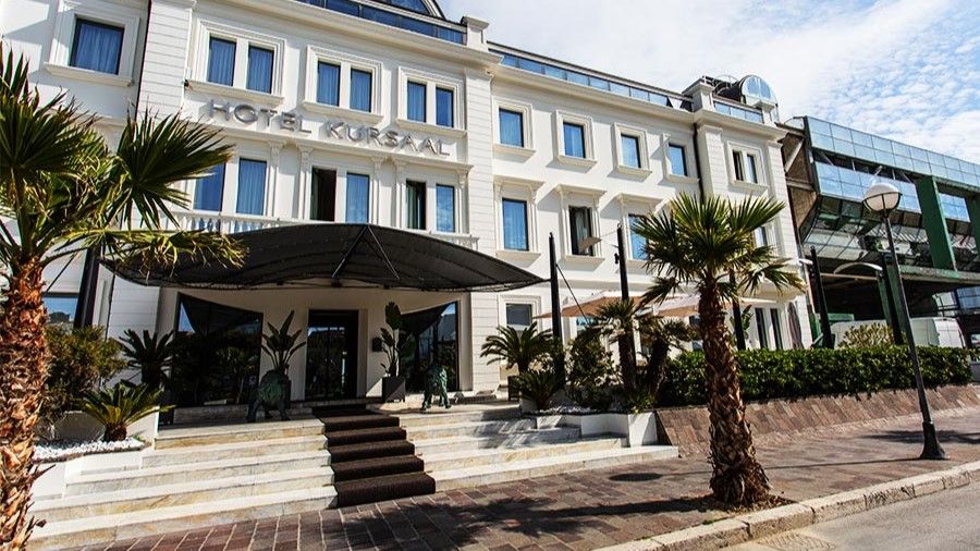 Außenansicht des Hotel Kursaal, elegantes weißes Gebäude mit Palmen und Eingangstreppe.