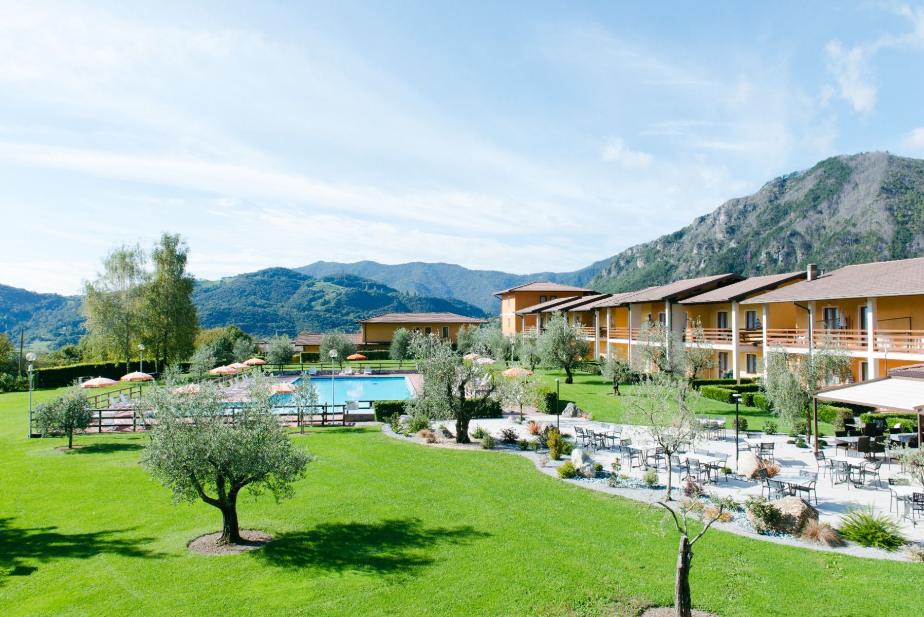 Außenansicht der Hotelanlage La Pertica mit Pool, Sonnenschirmen und Garten, eingebettet in eine Berglandschaft.
