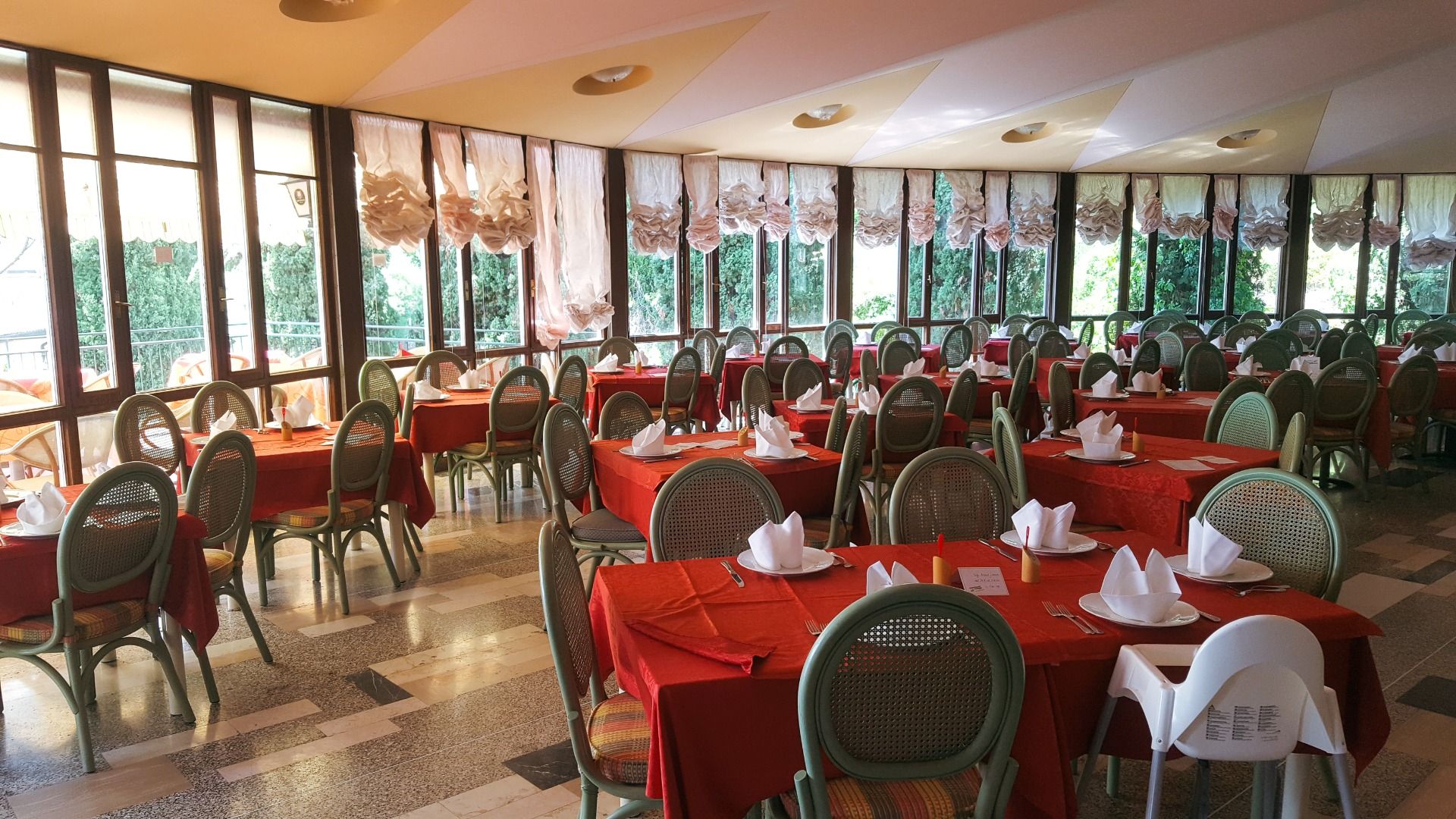 Restaurantbereich mit roten Tischdecken, grünen Stühlen und großen Fenstern, die einen Ausblick ins Grüne bieten.
