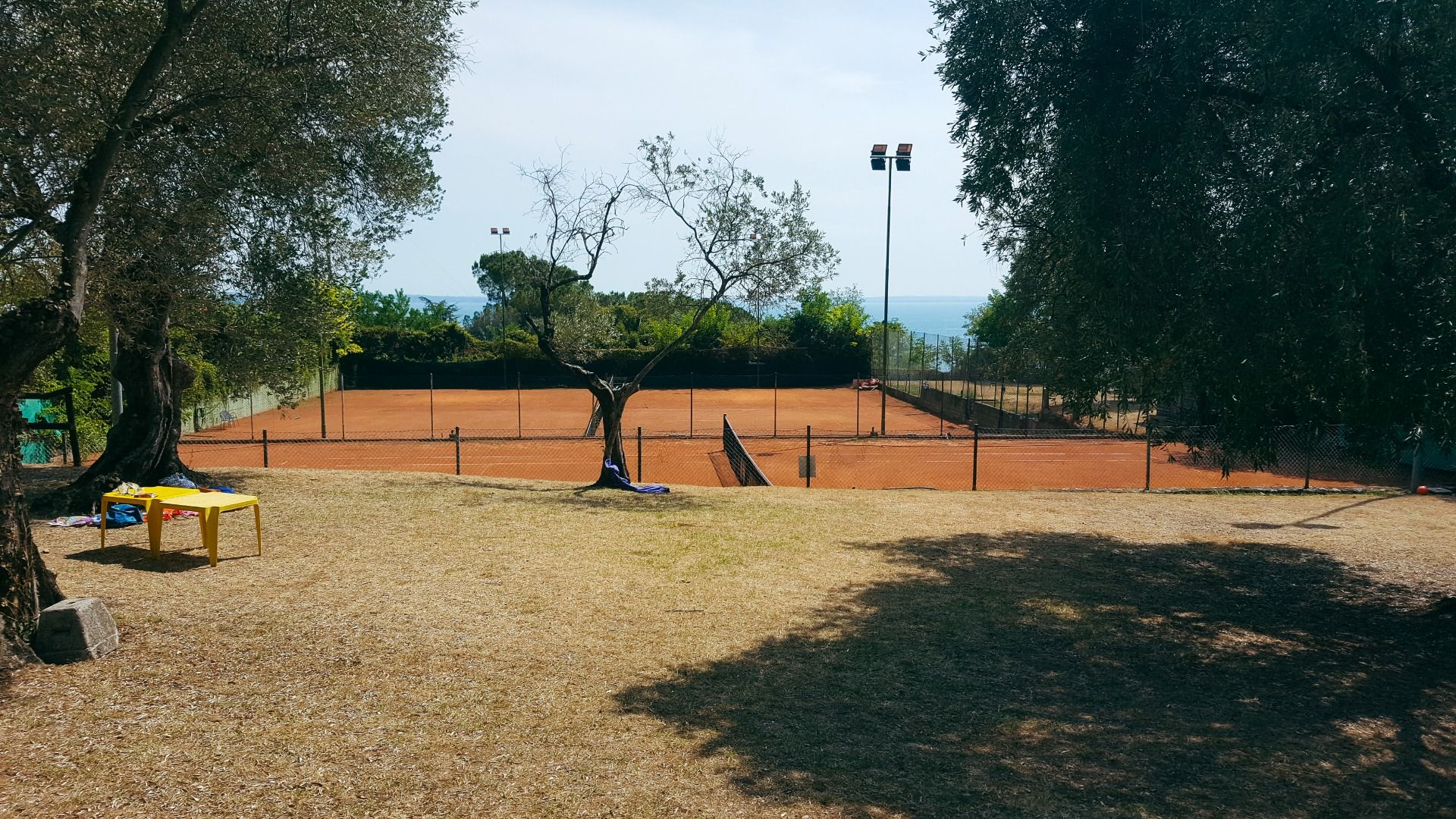 Blick auf einen Tennisplatz mit rotem Sandbelag, umgeben von Bäumen.
