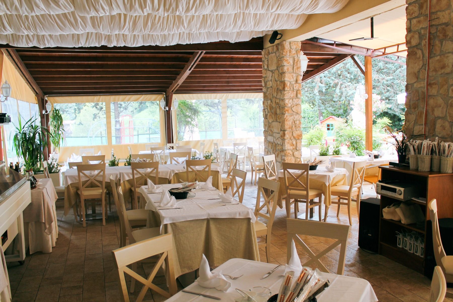 Überdachter Restaurantbereich mit Holzbalken, Steinwänden und gemütlicher Atmosphäre.
