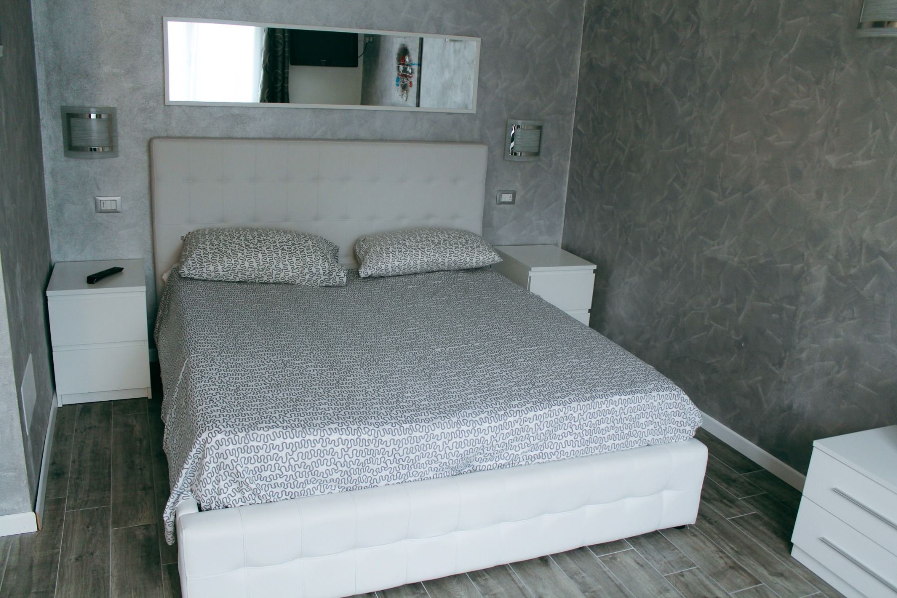 Modernes Hotelzimmer mit grauen Wänden, weißem Bett und minimalistischer Einrichtung.
