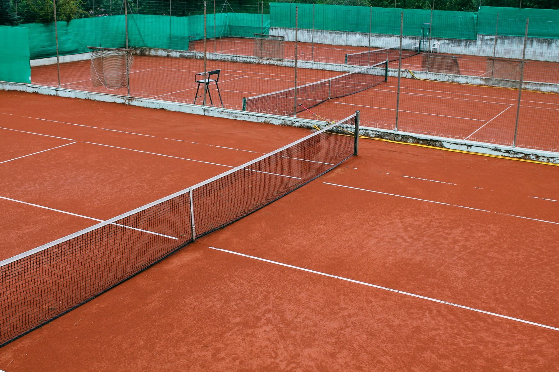 Tennisplatz mit rotem Sandbelag, Netz und Zaun.