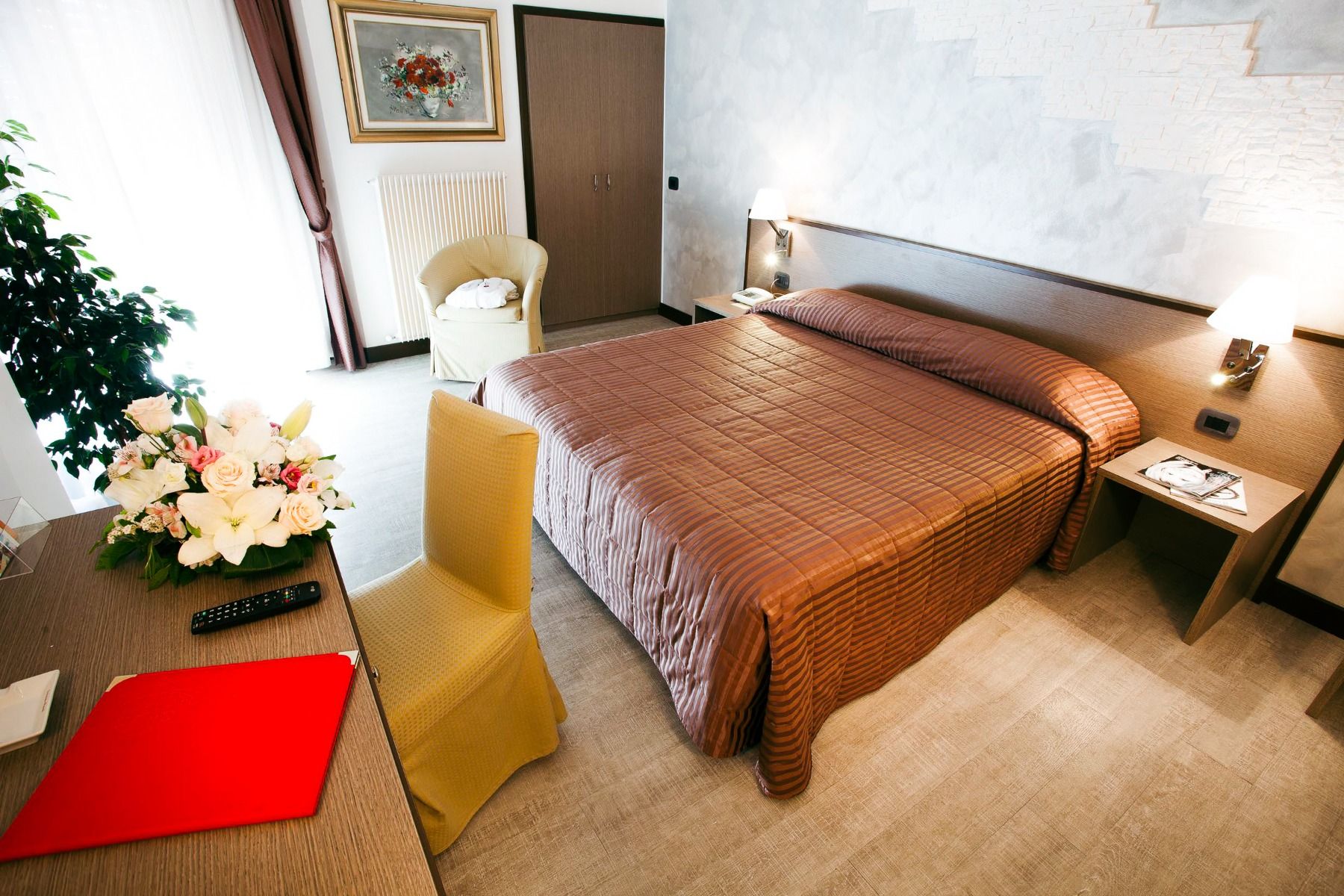 Modern eingerichtetes Hotelzimmer mit Doppelbett, Wanddekoration und Blumenstrauß.