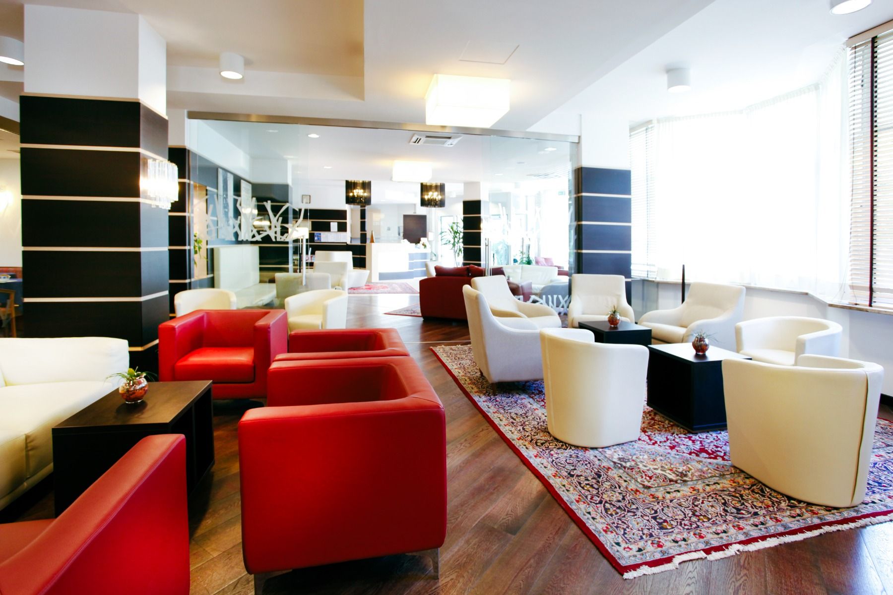 Lounge-Bereich im Hotel mit roten und weißen Sesseln, Couchtischen und Teppich.