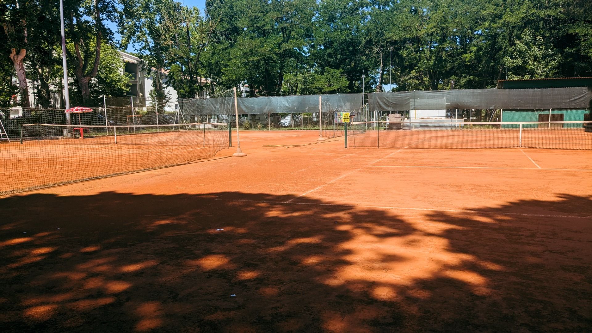 Roter Sand-Tennisplatz, von Bäumen umgeben,.