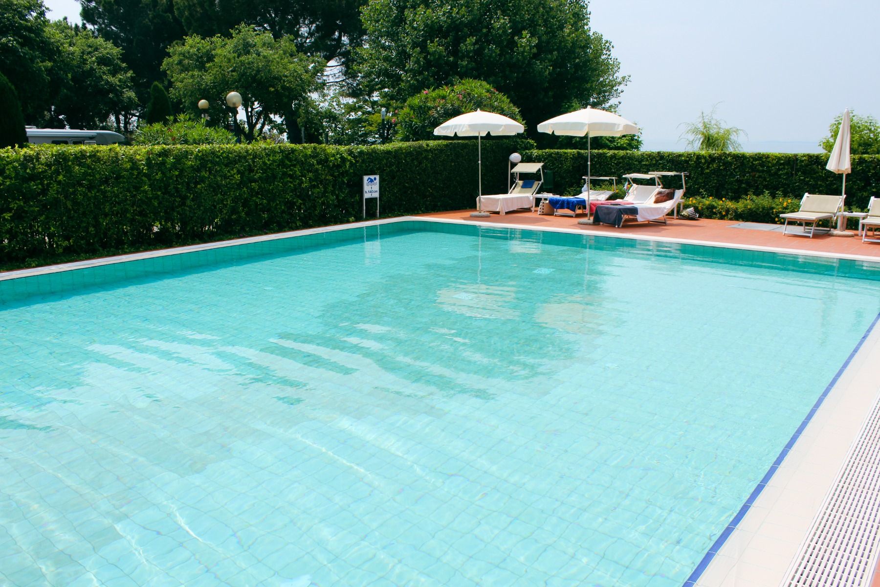 Außenpool des Hotel Sportsman mit Sonnenliegen und Sonnenschirmen, umgeben von Hecken und Bäumen.