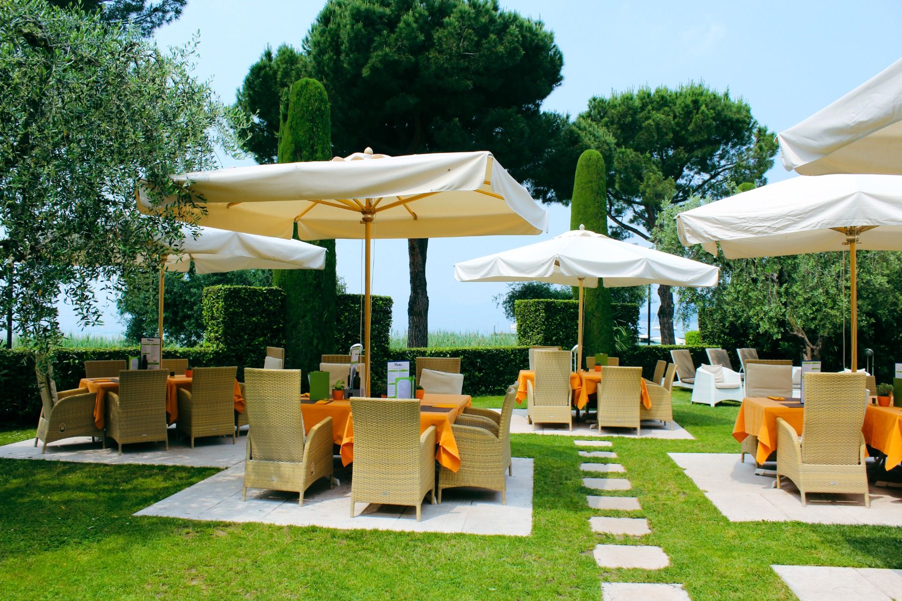 Gartenrestaurant des Hotel Sportsman mit Rattanmöbeln, Sonnenschirmen und gedeckten Tischen auf gepflegtem Rasen.