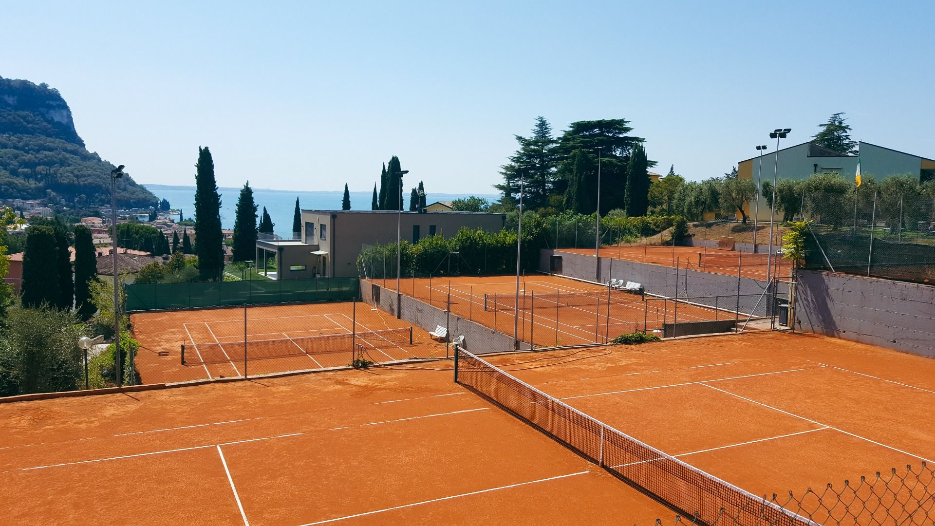 Tennisplätze auf Sand mit Blick auf den Gardasee, Zypressen und mediterraner Vegetation.