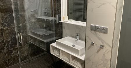 Das Hotel Biograf besticht durch eine hellgelbe und pfirsichfarbene Fassade, auff&auml;llige Beschilderungen f&uuml;r das Hotel, das Restaurant und das Caf&eacute; sowie Fenster auf beiden Etagen; links ist ein blaues Stra&szlig;enschild zu sehen.