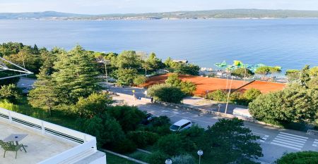 Hinter üppig grünen Bäumen und Sträuchern erhebt sich das hohe, moderne, weiße Gebäude des Hotels Omorika. Eine lange Steintreppe führt hinauf zum Eingang, an dessen Vorderseite ein blaues „Hotel Omorika“-Schild angebracht ist.