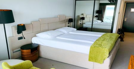 Hinter üppig grünen Bäumen und Sträuchern erhebt sich das hohe, moderne, weiße Gebäude des Hotels Omorika. Eine lange Steintreppe führt hinauf zum Eingang, an dessen Vorderseite ein blaues „Hotel Omorika“-Schild angebracht ist.
