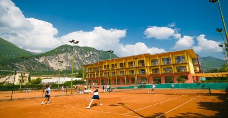 Sand-Tennisplatz mit Spielern, Hotel im Hintergrund und Bergkulisse.