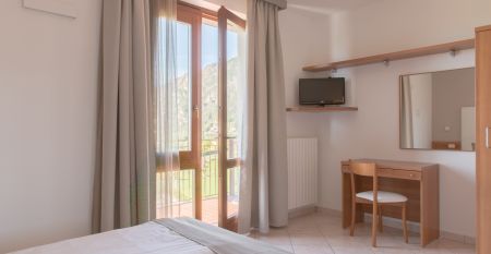 Außenansicht der Hotelanlage La Pertica mit Pool, Sonnenschirmen und Garten, eingebettet in eine Berglandschaft.