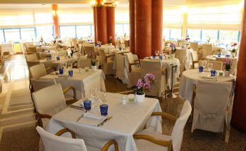 Gartenrestaurant des Hotel Sportsman mit Rattanmöbeln, Sonnenschirmen und gedeckten Tischen auf gepflegtem Rasen.