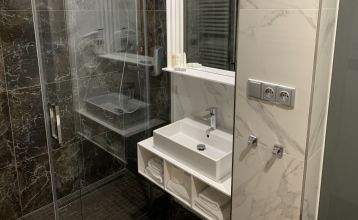 Das Hotel Biograf besticht durch eine hellgelbe und pfirsichfarbene Fassade, auffällige Beschilderungen für das Hotel, das Restaurant und das Café sowie Fenster auf beiden Etagen; links ist ein blaues Straßenschild zu sehen.