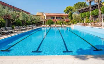 Eingang des Sporthotels Olimpo mit Steinfassade, Hotelname und Sternenmarkierung, umgeben von Pflanzen und Bäumen.