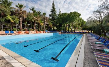 Eingang des Sporthotels Olimpo mit Steinfassade, Hotelname und Sternenmarkierung, umgeben von Pflanzen und Bäumen.