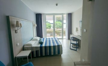 Außenansicht des modernen Hotel Capo Nord mit runder Architektur, Holzverkleidung und Balkonen, eingebettet in eine grüne Gartenlandschaft.