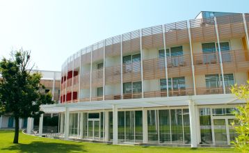 Außenansicht des modernen Hotel Capo Nord mit runder Architektur, Holzverkleidung und Balkonen, eingebettet in eine grüne Gartenlandschaft.