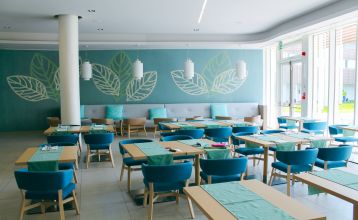 Außenansicht des modernen Hotel Capo Nord mit runder Architektur, Holzverkleidung und Balkonen, eingebettet in eine grüne Gartenlandschaft.