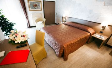 Außenbereich eines Hotels mit rosa Fassade, Balkonen und Palmen, sowie Sitzgelegenheiten im Garten.