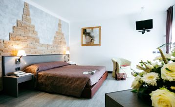 Außenbereich eines Hotels mit rosa Fassade, Balkonen und Palmen, sowie Sitzgelegenheiten im Garten.