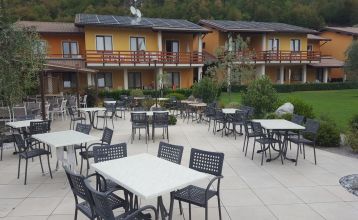 Außenansicht der Hotelanlage La Pertica mit Pool, Sonnenschirmen und Garten, eingebettet in eine Berglandschaft.