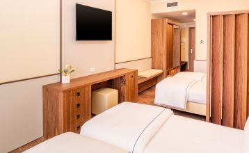 Eingang des Sporthotels Olimpo mit Steinfassade, Hotelname und Sternenmarkierung, umgeben von Pflanzen und Bäumen.